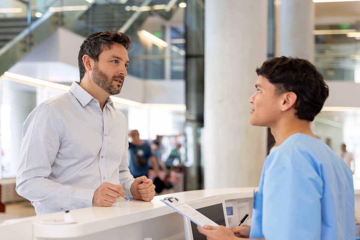 Patient talking to male medical administrative assistant at the nurse station 