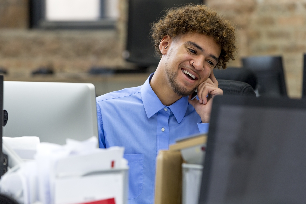Young man on the phone while in front of his computer screen.