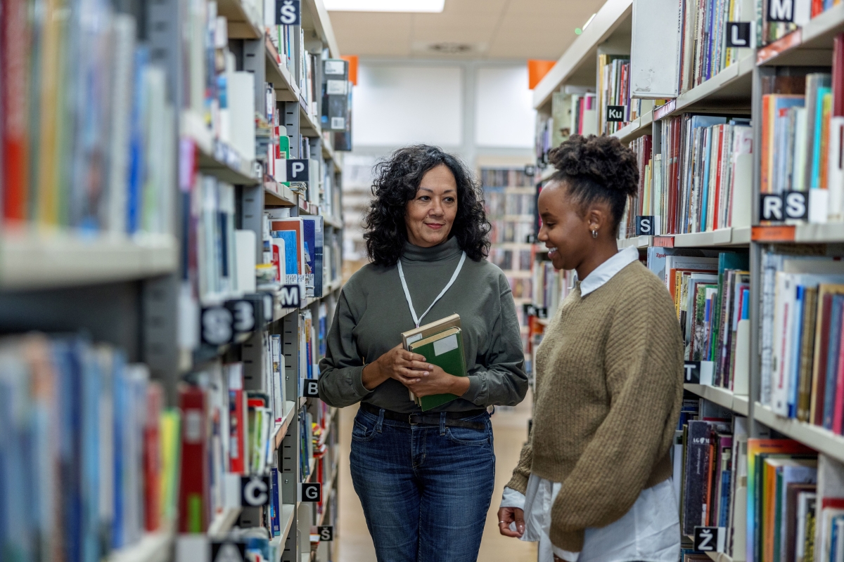 Black female librarian helping a young black female college student find a book 