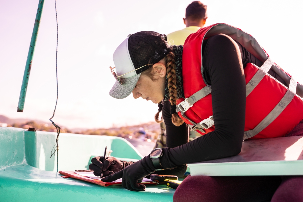 Female marine biologist writing data on top of a boat