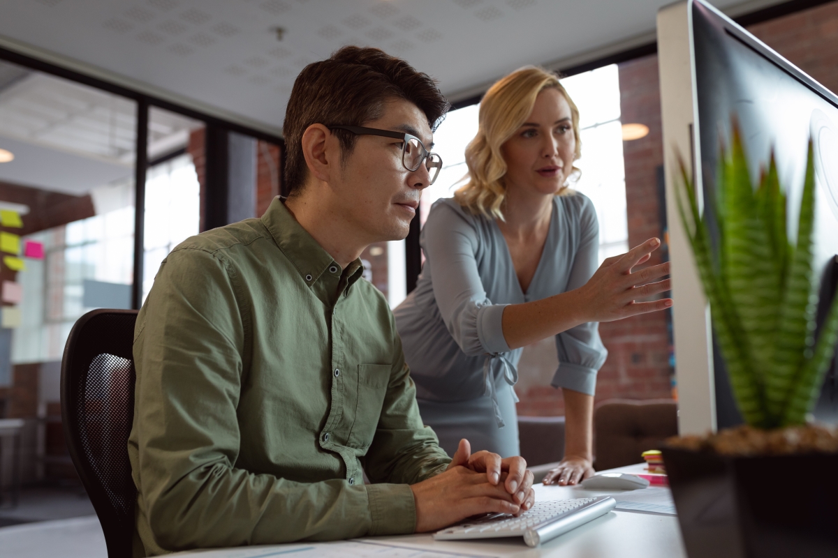 Diverse male and female colleague looking at computer screen and discussing at desk in office 