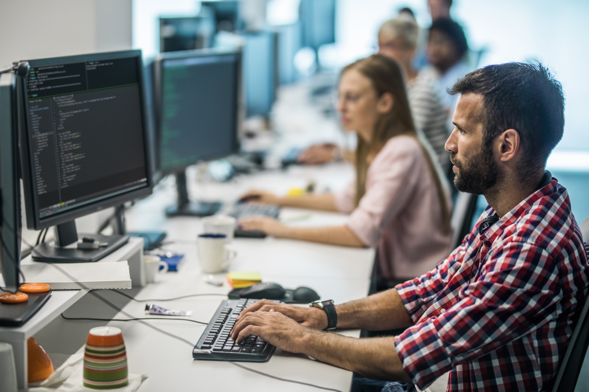 Young computer programmer developing new software while working on desktop PC in the office. 