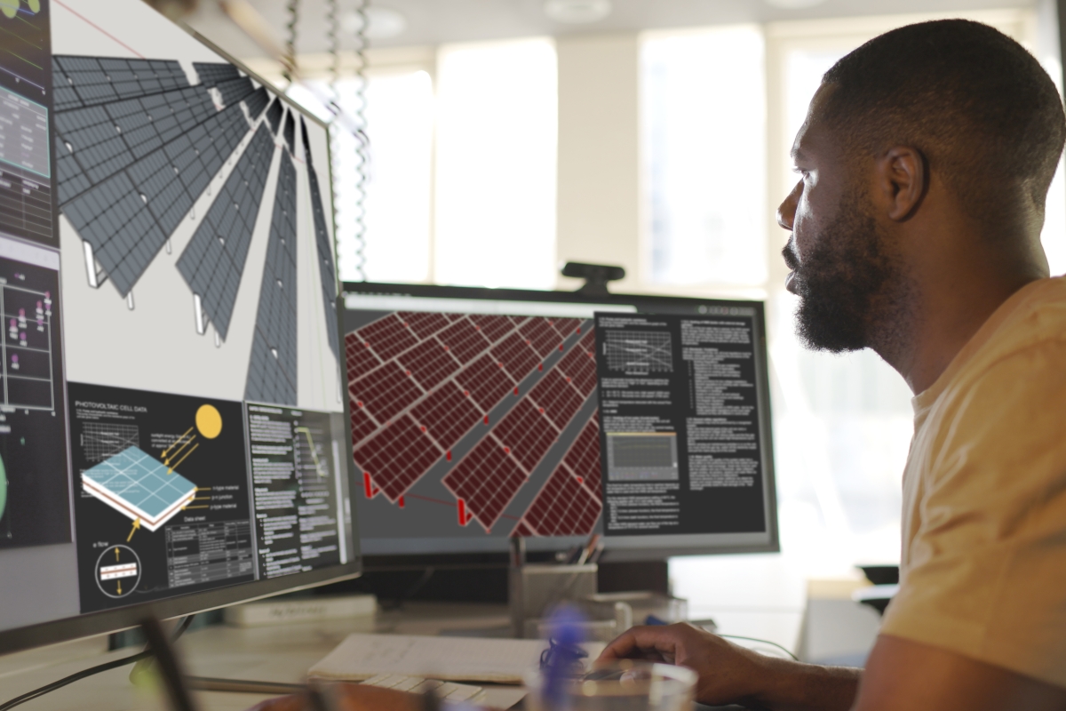 Black male engineer working on a solar field design on a computer with multiple screens
