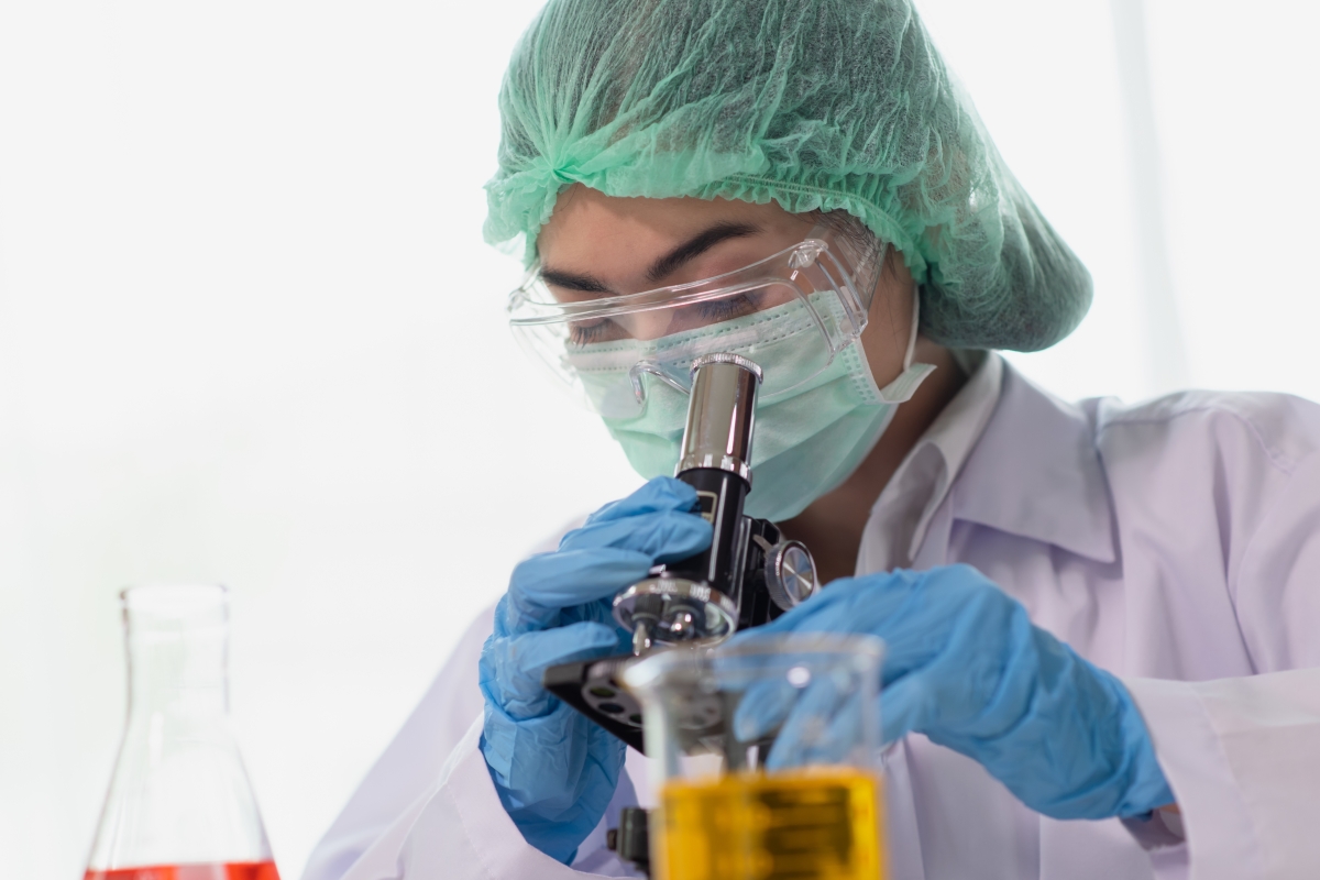 female scientist wearing protective clothing looking through microscope in a lab