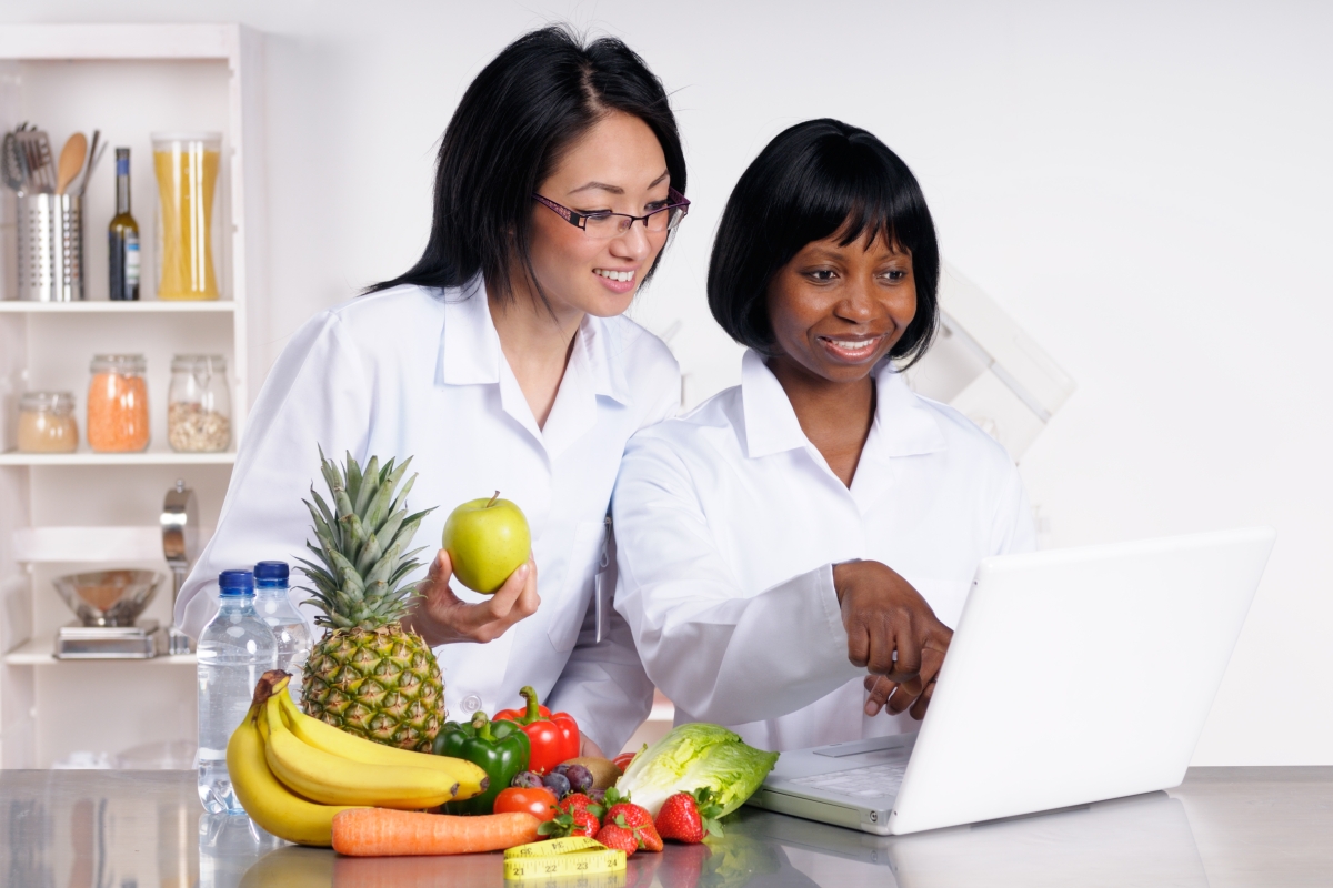 Two diverse female dietitians working on a laptop with a selection of fruit and vegetables