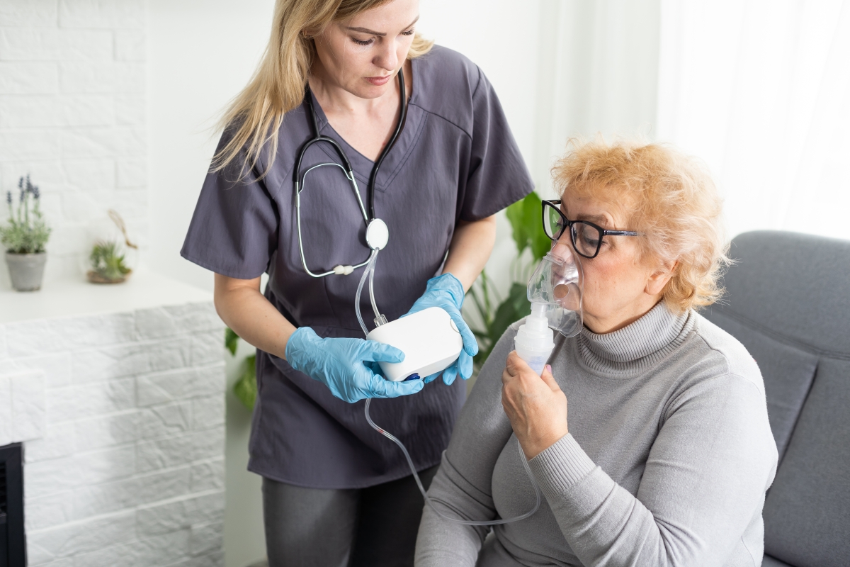 Young respiratory therapist putting oxygen mask on face of her elderly female patient 