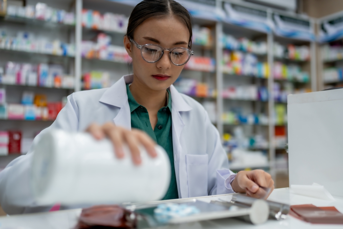 Young Asian female pharmacy tech assistant is sorting medications. 