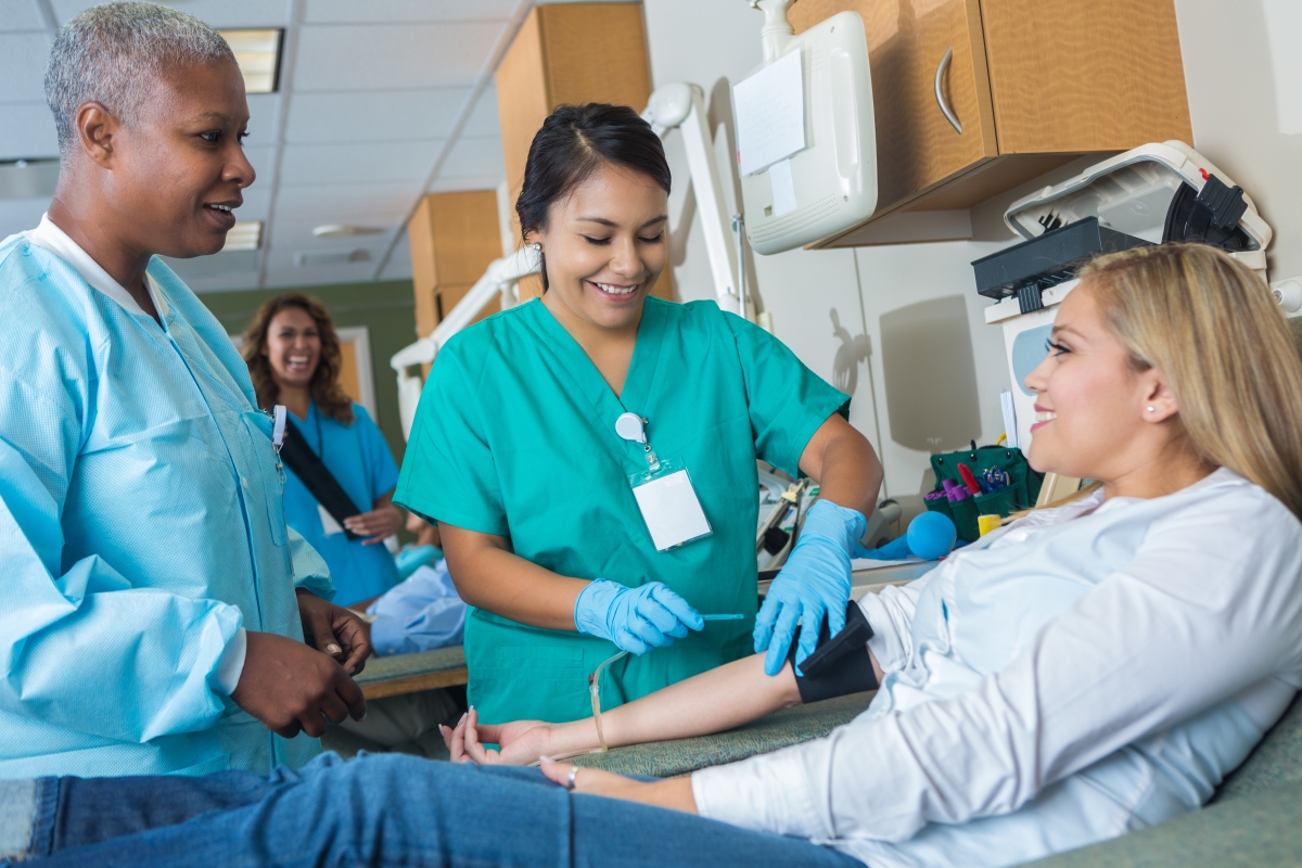 Blood donor clinic assistant collects blood from blood donor