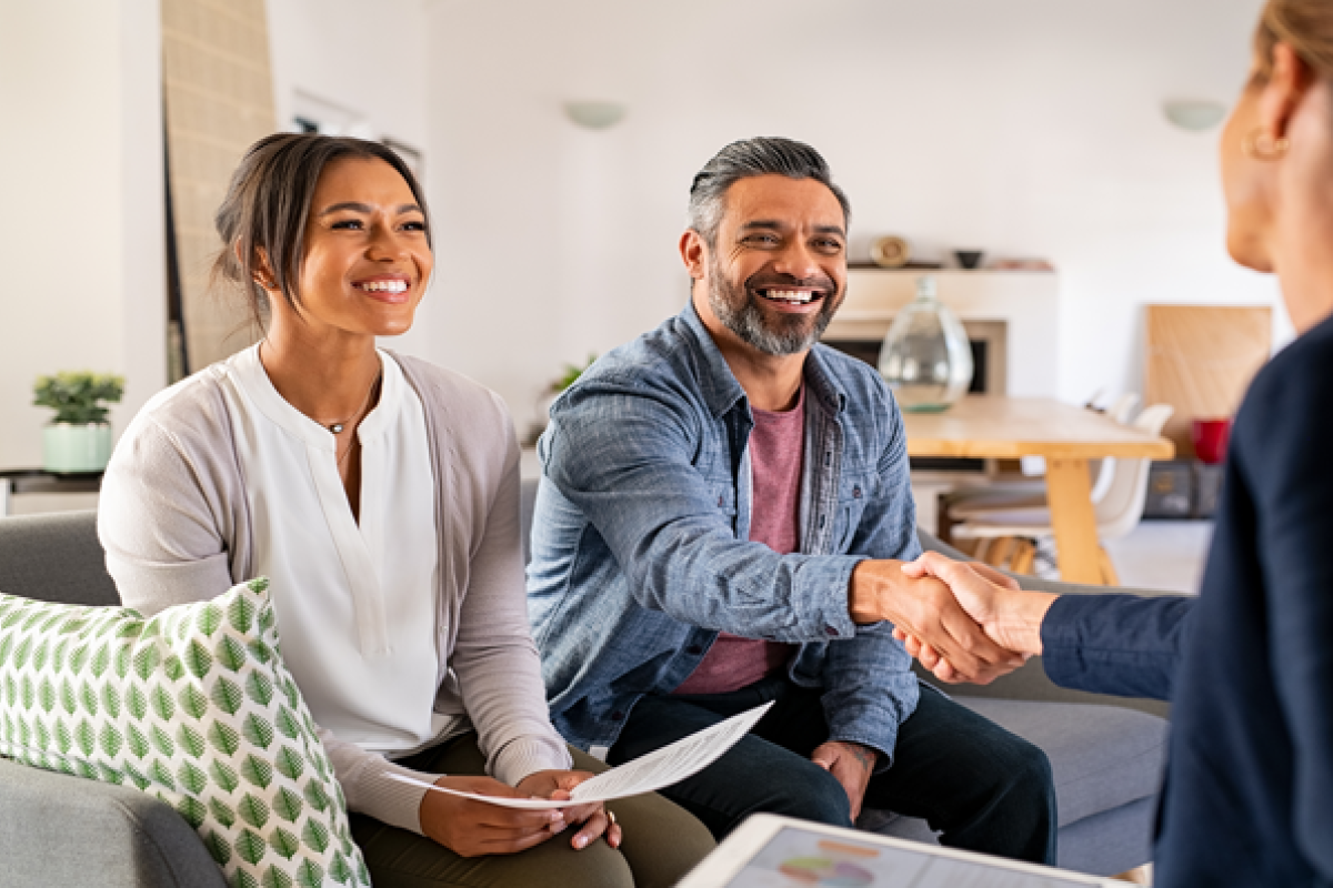 Multiethnic couple handshake with financial advisor at home.