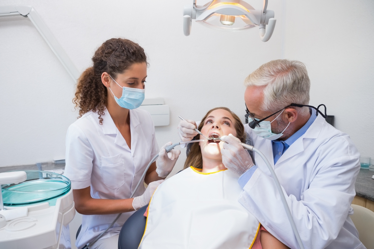 Mature dentist with female dental assistant examining patient's mouth.