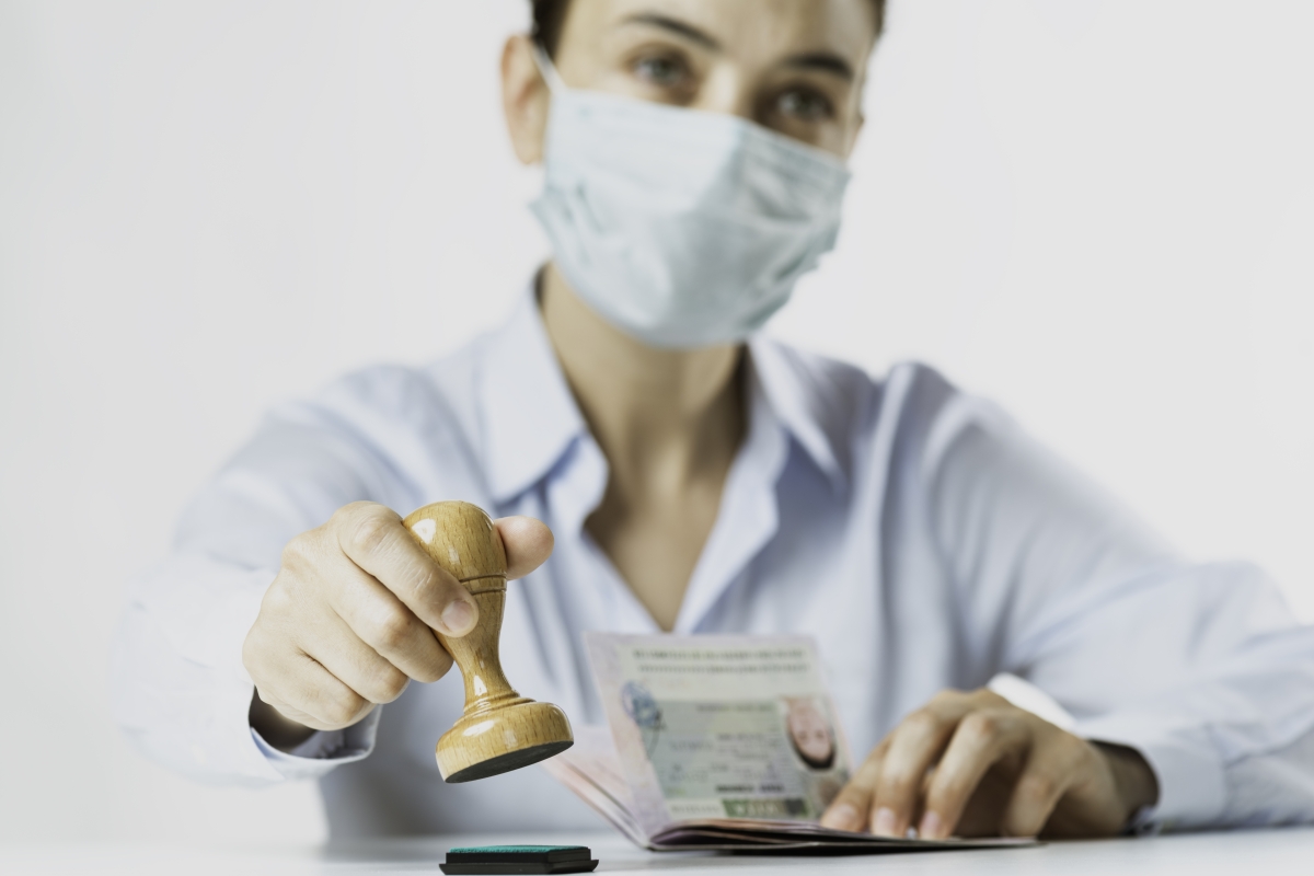 Caucasian woman officer wearing protective face mask is about to stamp on passport.