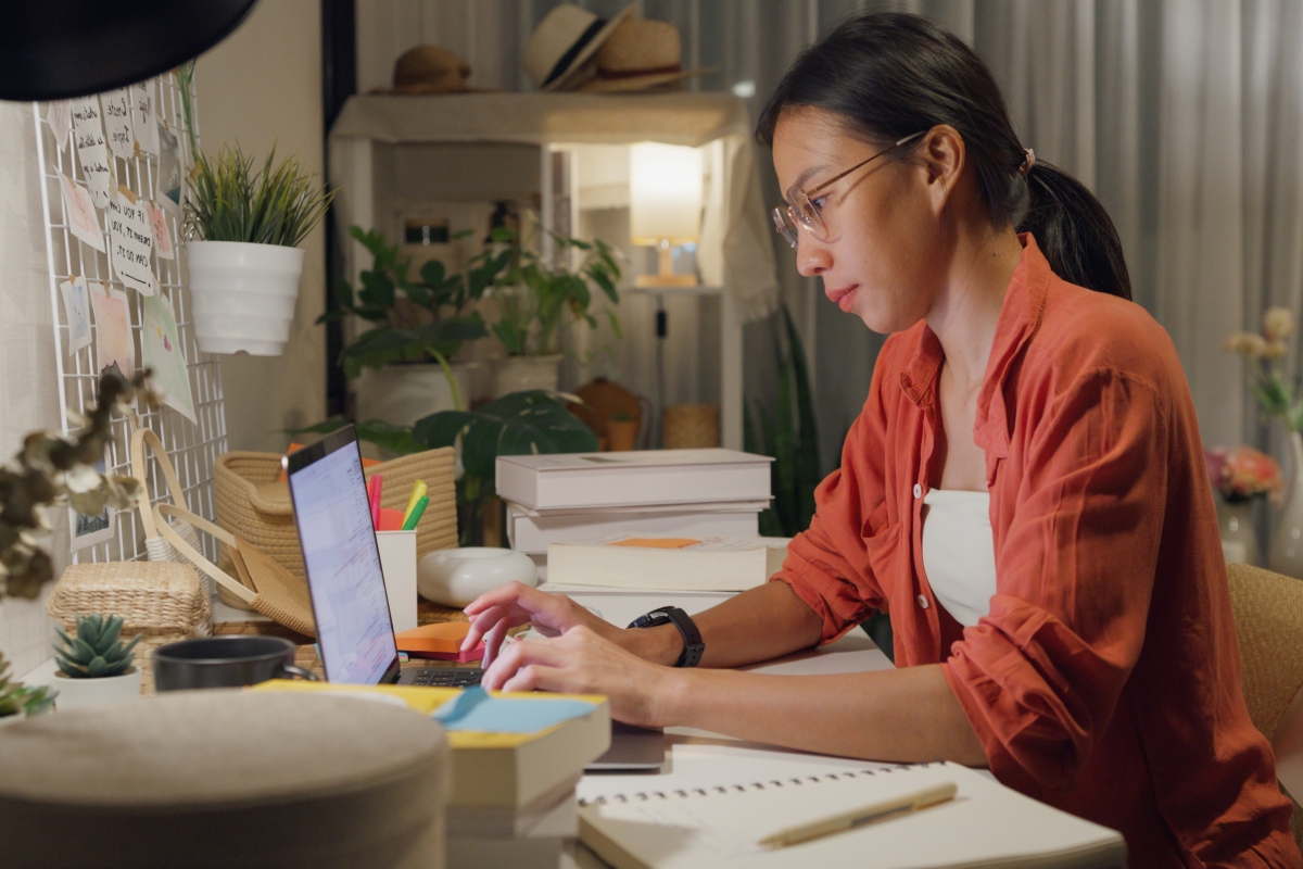 Young Asian woman at desk working on laptop.