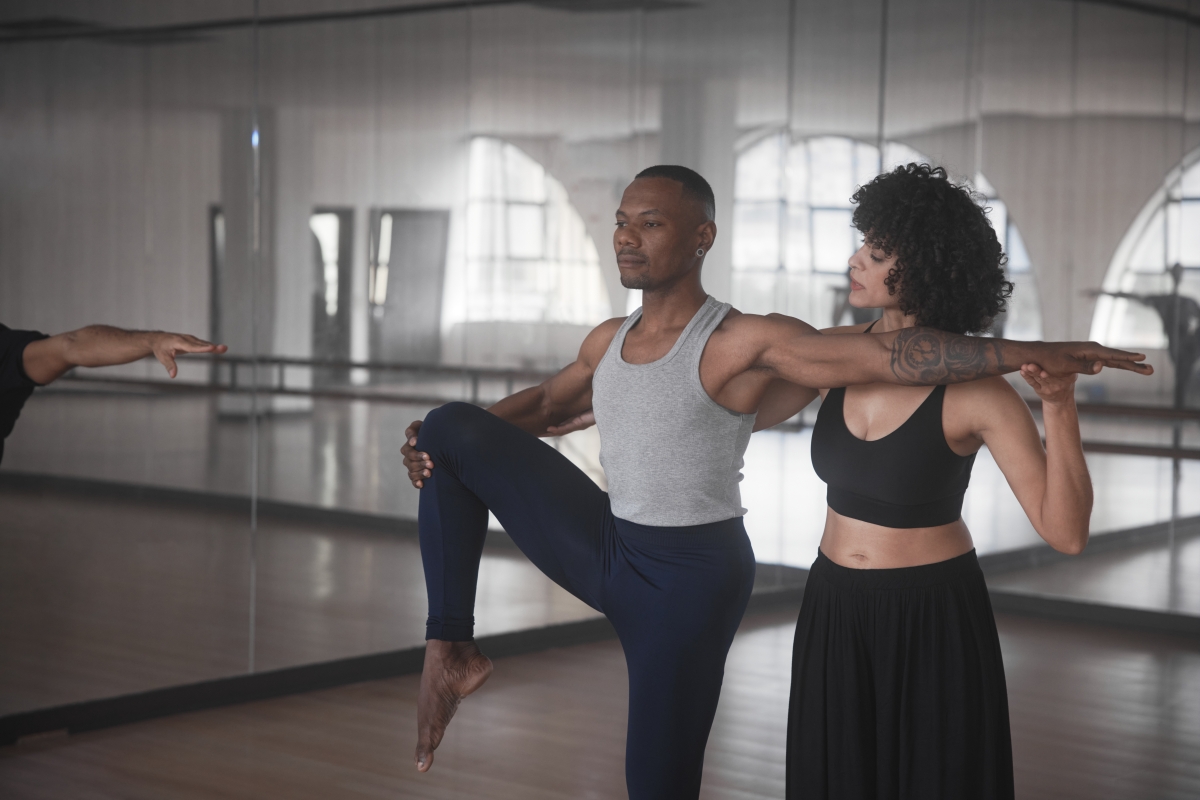 Black female dance instructor and male student working on form during dance class