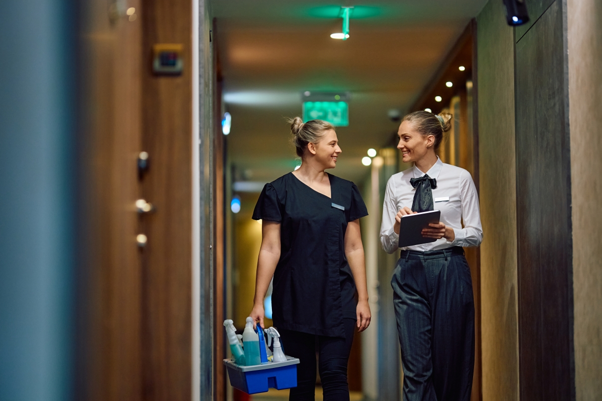 Housekeeping executive using touchpad while communicating with chambermaid in a hotel hallway.