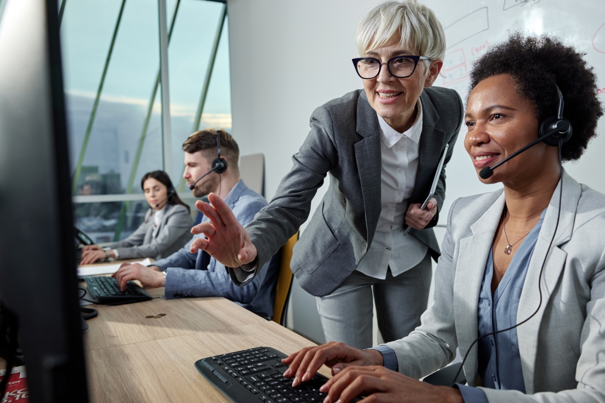 Mature worker assisting her employee while working on computer in a contact centre.