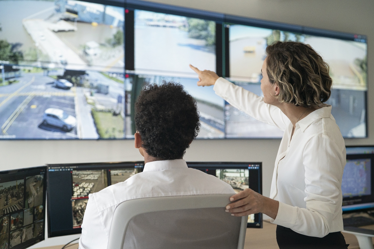Female and male security coworkers discussing while looking at video wall.