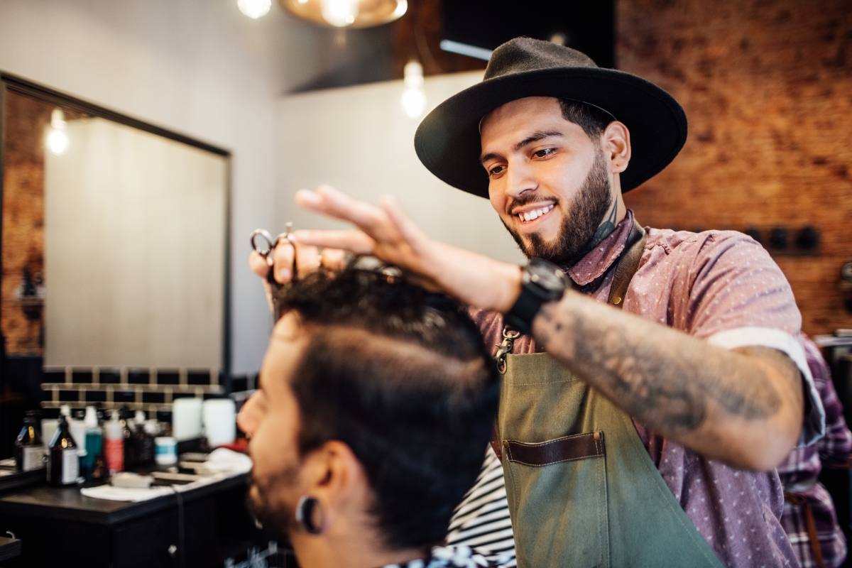 Male barber cutting customer's hair in salon.