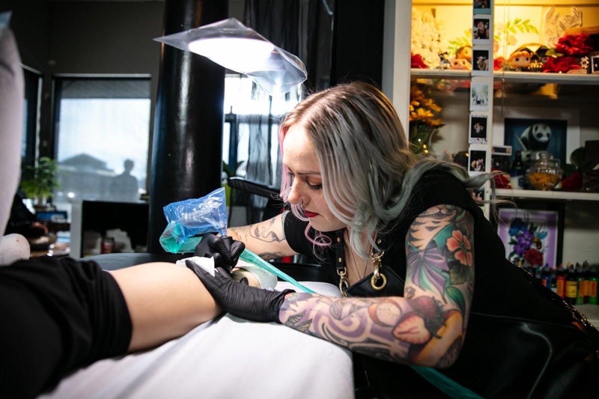 Female tattoo artist creating a tattoo on a client leg.  