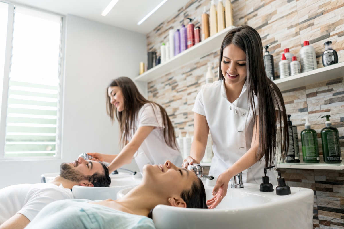 Relaxed customers with eyes closed getting their hair washed by two young female hairstylist assistants..