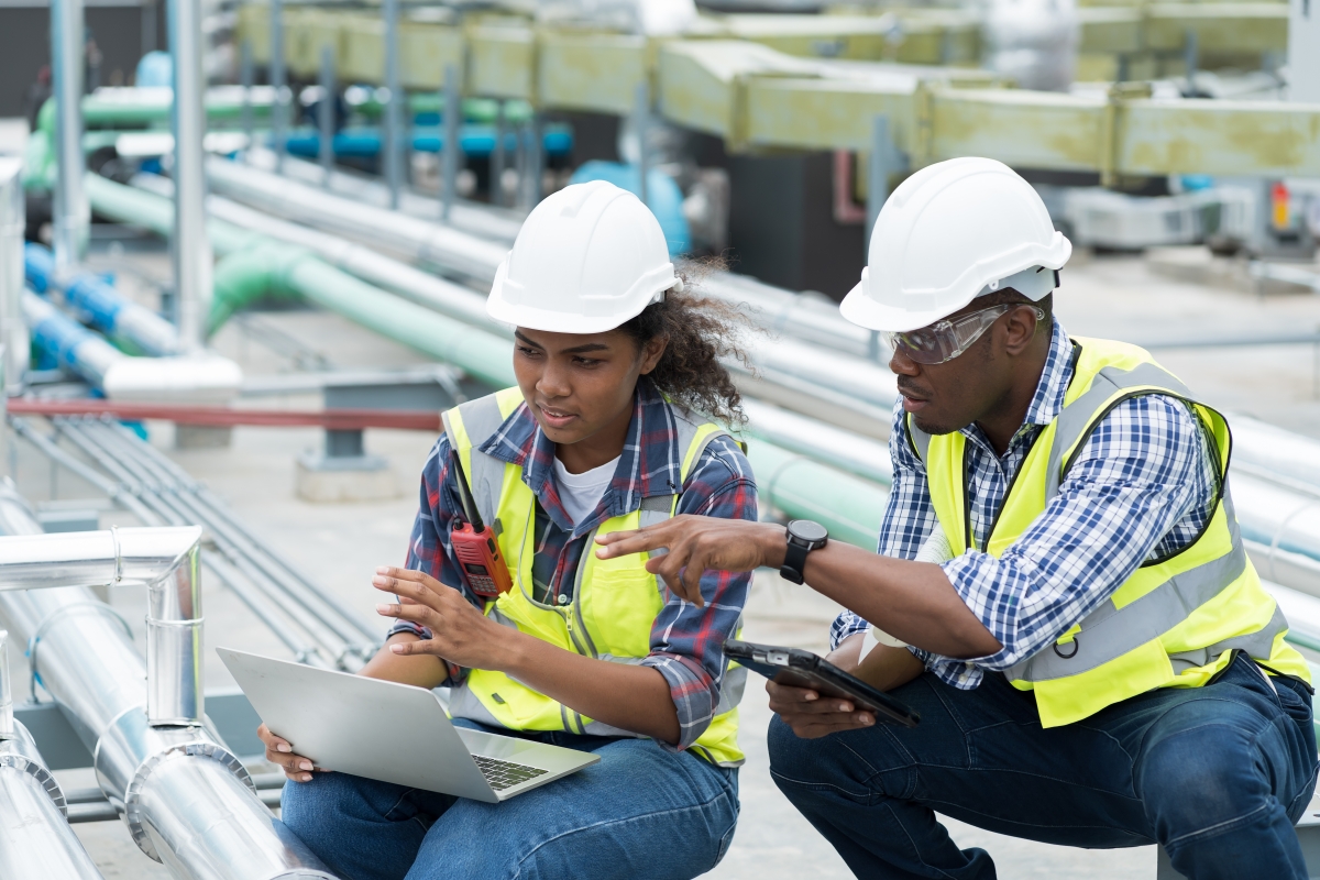 Male and female trade contractors discussing sewer pipe maintenance on rooftop of building.