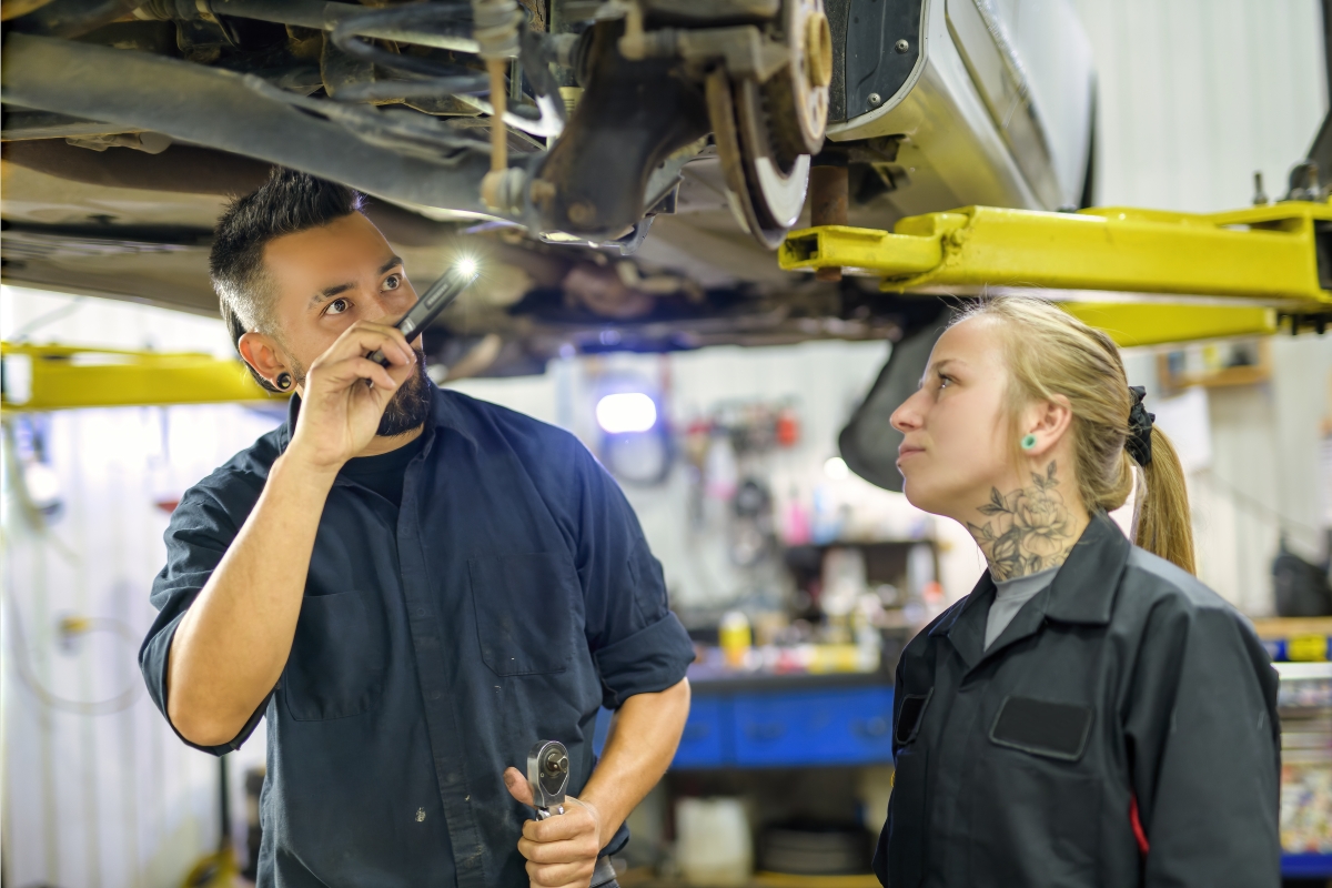 Male supervisor of a female mechanic inspecting her work on a car. 