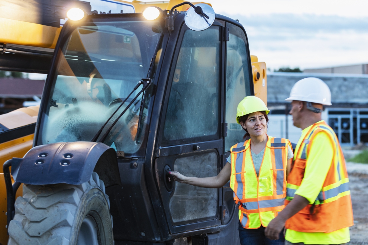 Male supervisor talking with female construction heavy equipment operator at job site.