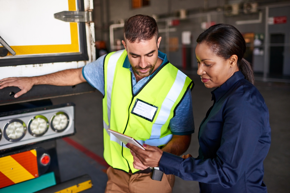 Female supervisor holding a digital tablet and talking to a male truck driver on the warehouse loading dock.
