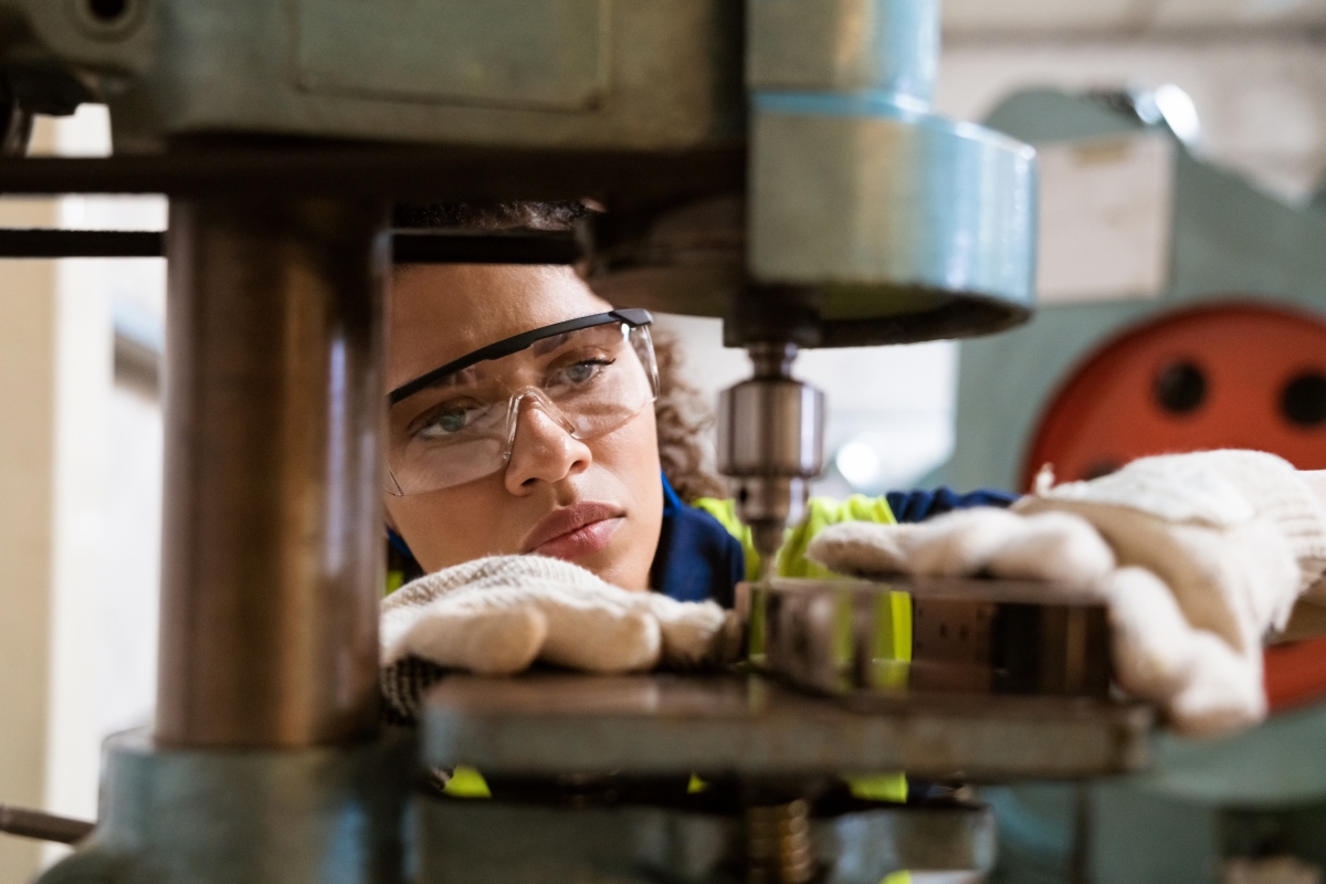 Female machinist wearing safety gear working on a yoke machine in a manufacturing factory..