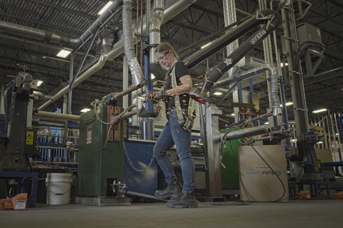 Female sheet metal worker working on machine in factory.