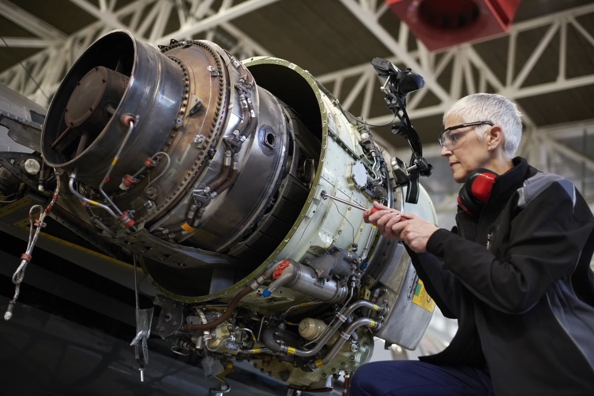 Mature female mechanic in the hangar repairing and maintaining airplane jet engine.
