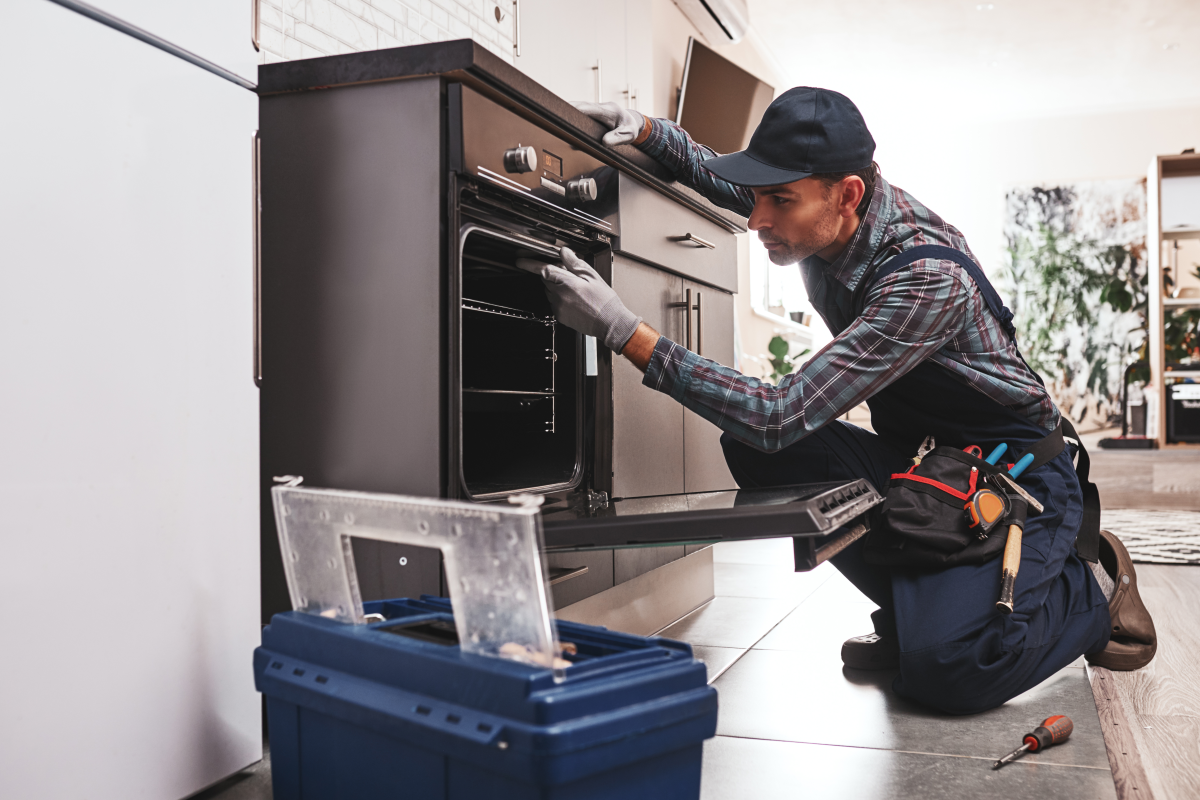 Male appliance service technician examining oven in kitchen.