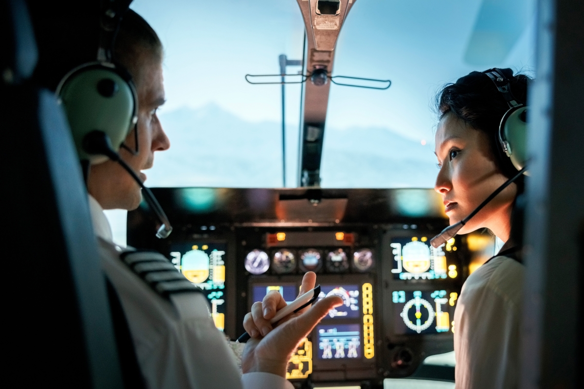 Male pilot talking to female co-pilot in helicopter cockpit. 