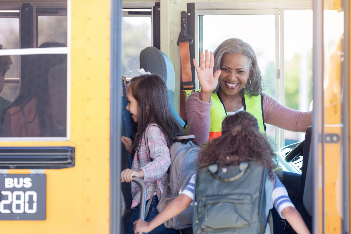 Black female bus driver high-fives children boarding bus.