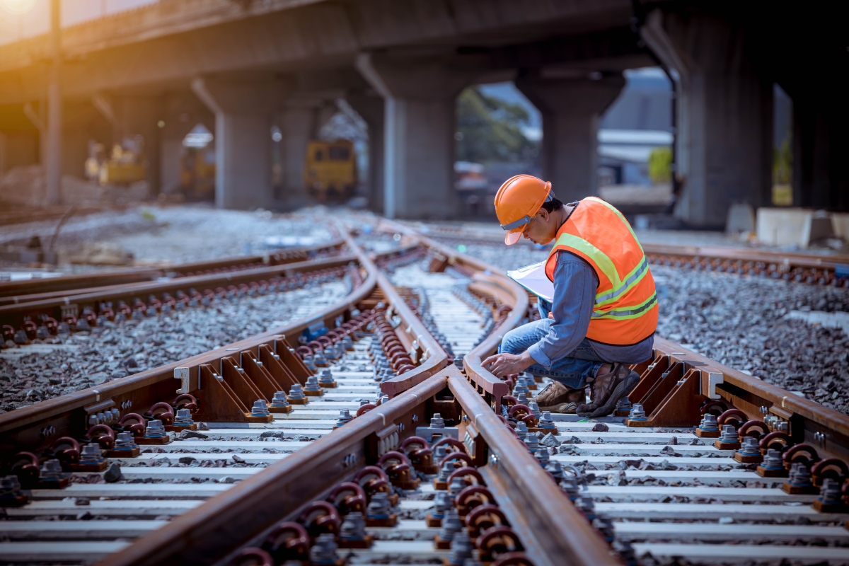 Male railway worker wearing safety gear inspecting railway switch.