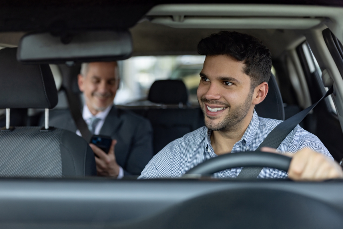 Smiling male driver transporting a business man in a crowdsourced taxi.