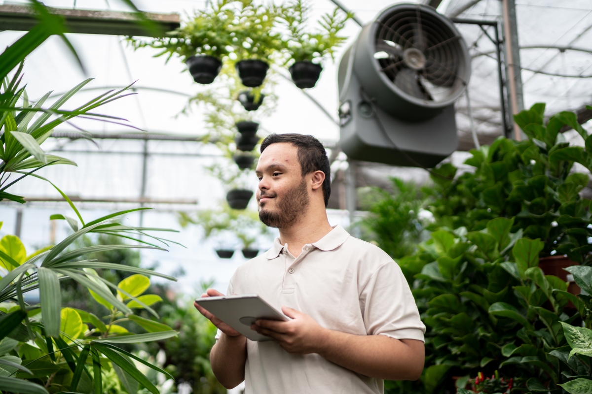 Young special needs man working using digital tablet in a garden center.