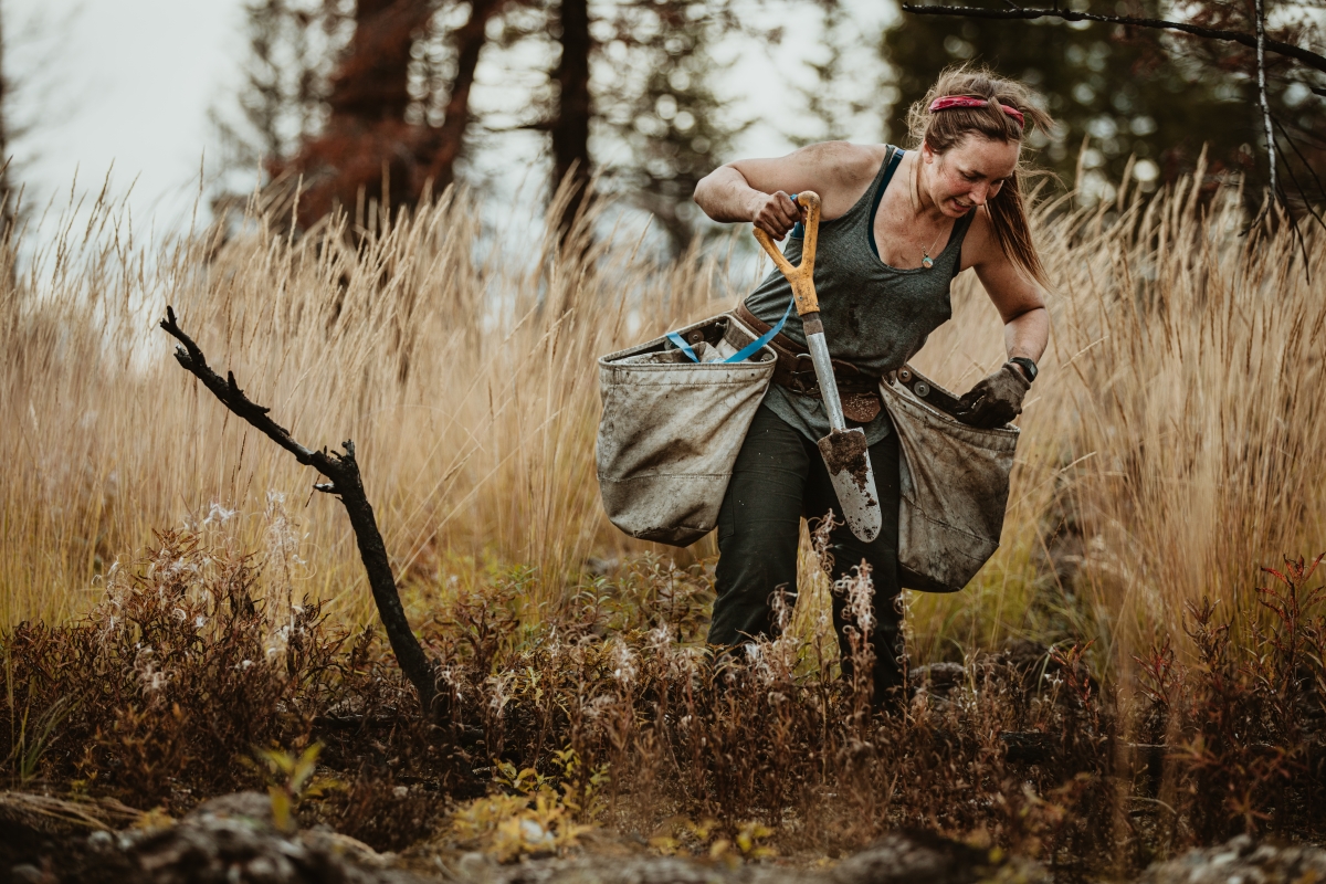 Woman digging hole in forest to plant saplings. 