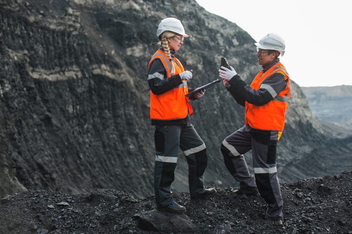 Male and female workers in safety gear examining coal at an open pit.