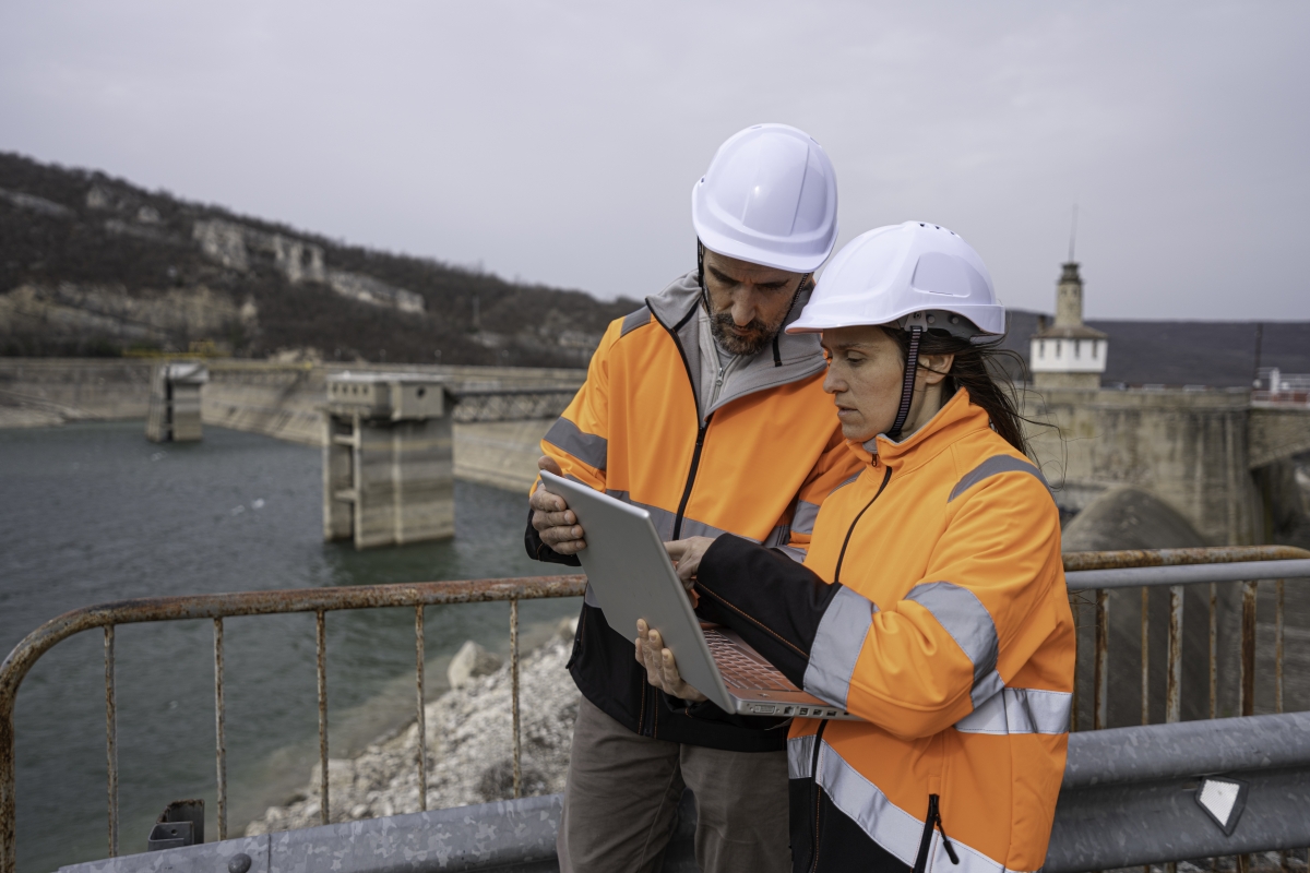 Male and female power engineers wearing safety gear working at a hydroelectric power plant. 