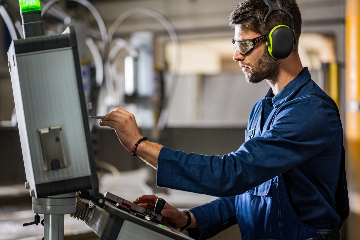 Caucasian male is operating a CNC control panel while wearing protective gear.