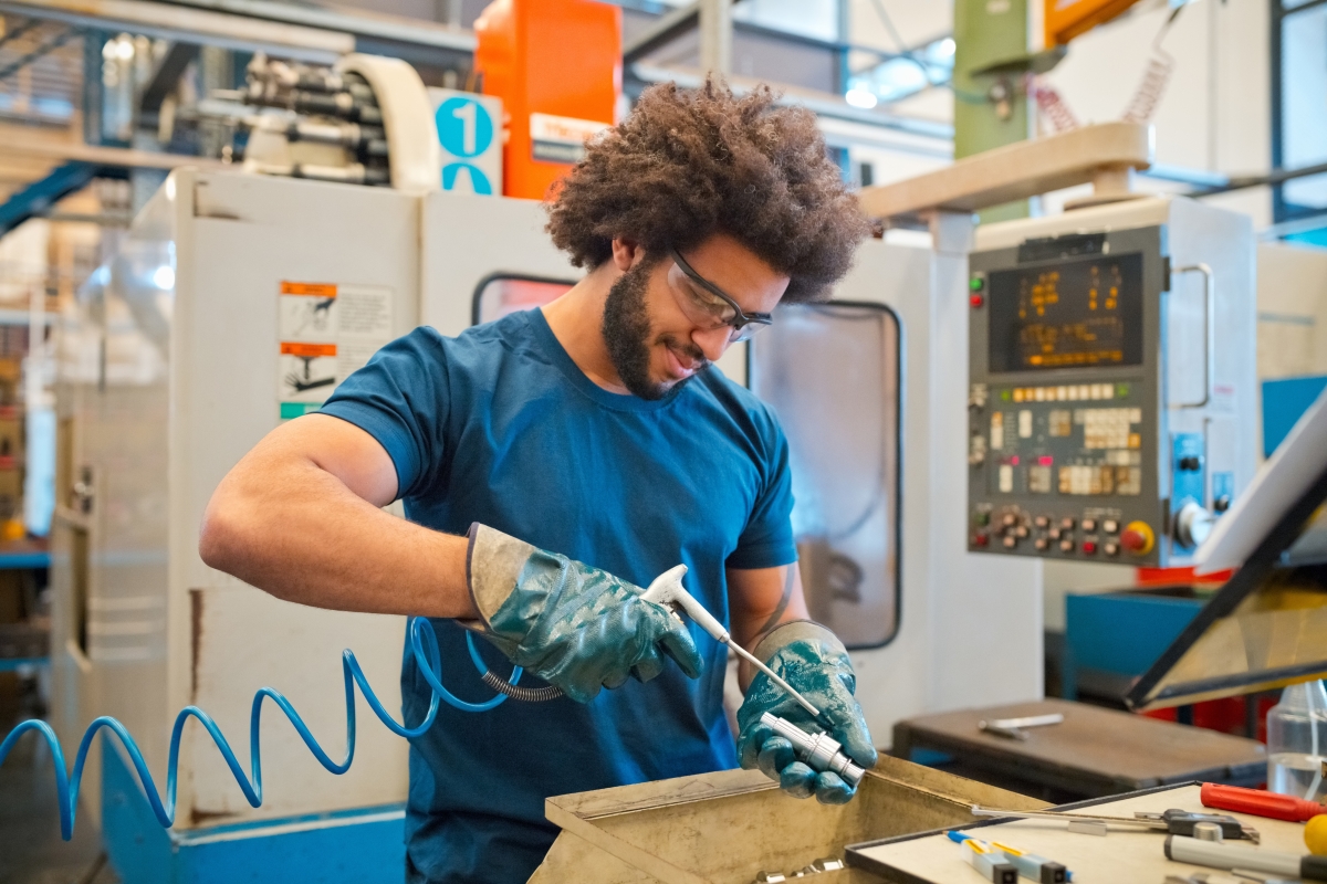 Young male technician wearing protective gear using machinery while working in factory.