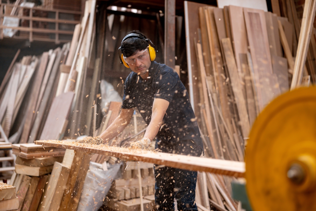 Male worker wearing protective workwear while sanding a plank of wood at a timber factory.