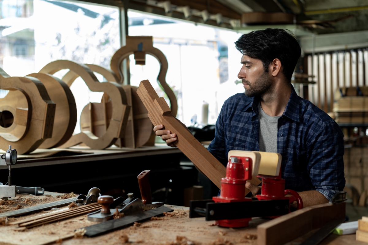 Male guitar luthier examines wood for acoustic guitar neck.