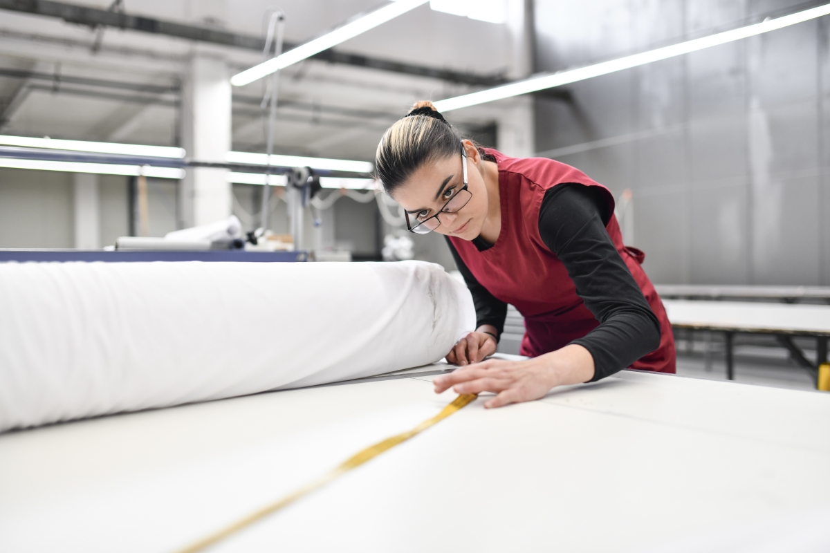 Focused female textile worker measuring fabric roll. 