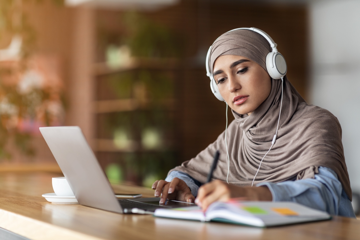 Young woman wearing headscarf and headphones studying at computer