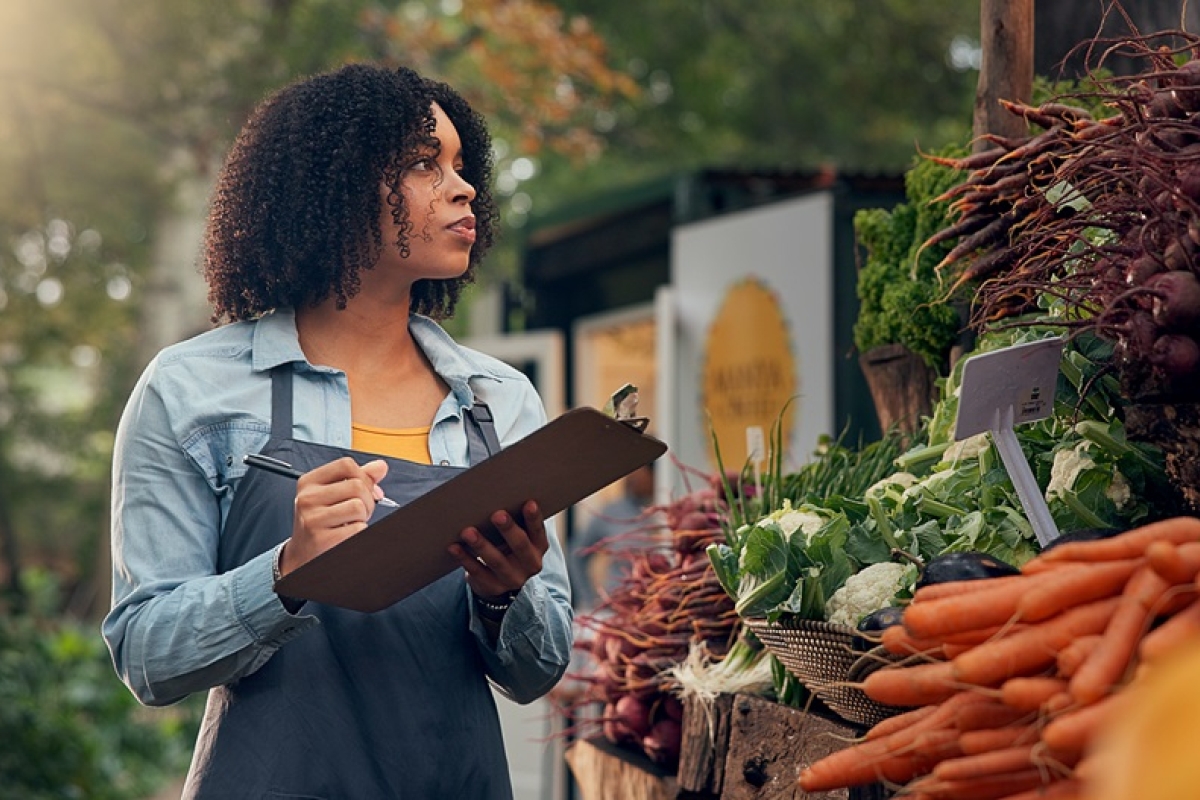 Black woman in apron taking inventory of vegetables to purchase