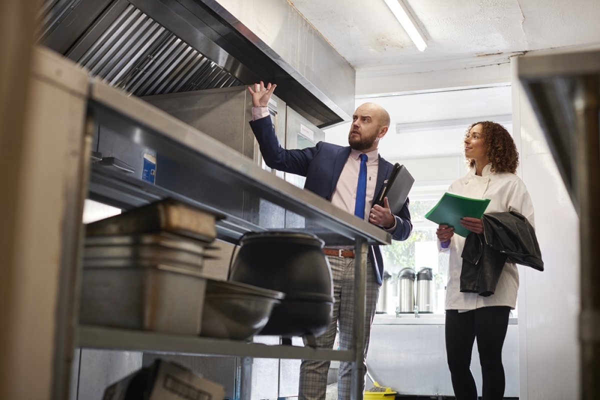 Male restaurant inspector inspecting kitchen with restaurant owner