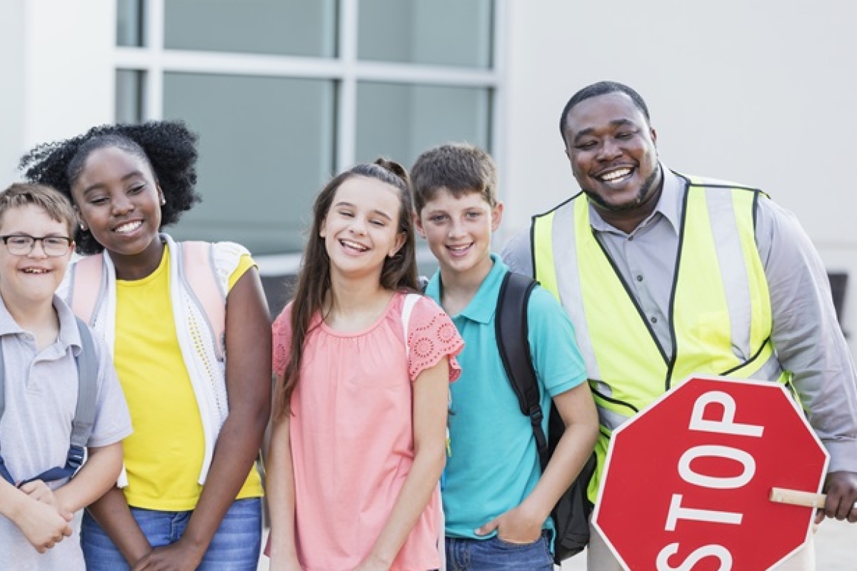 Black male crossing guard holding stop sign with diverse group of students