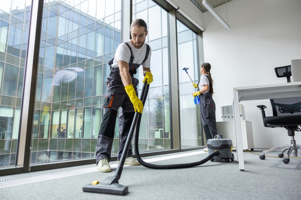 Male and female team of cleaners vacuuming and cleaning windows in officer