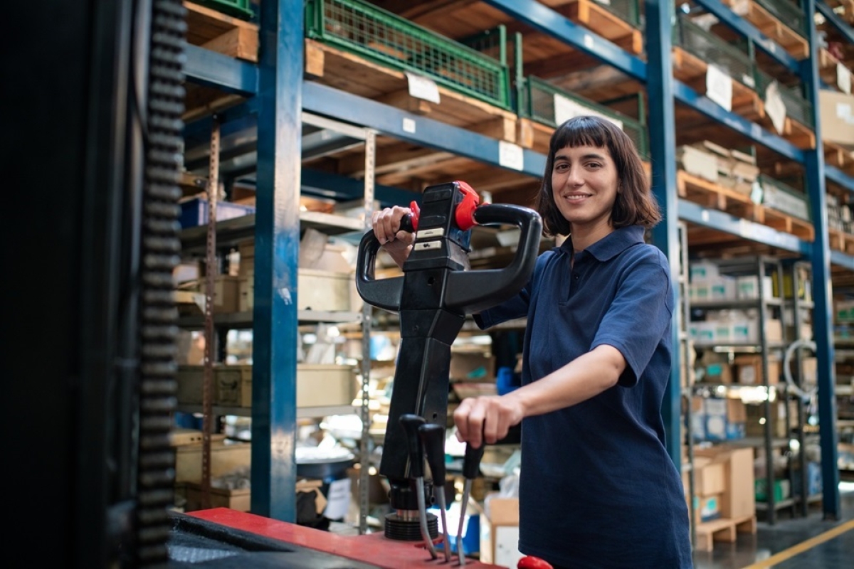 Young female material hander operating pallet jack in warehouse